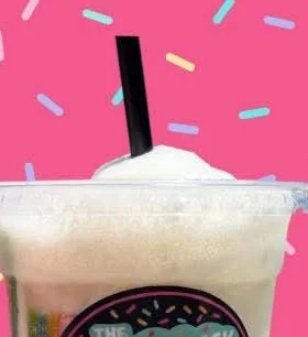 A Dairy Duck dirty soda in a clear cup with a black straw, topped with whipped cream