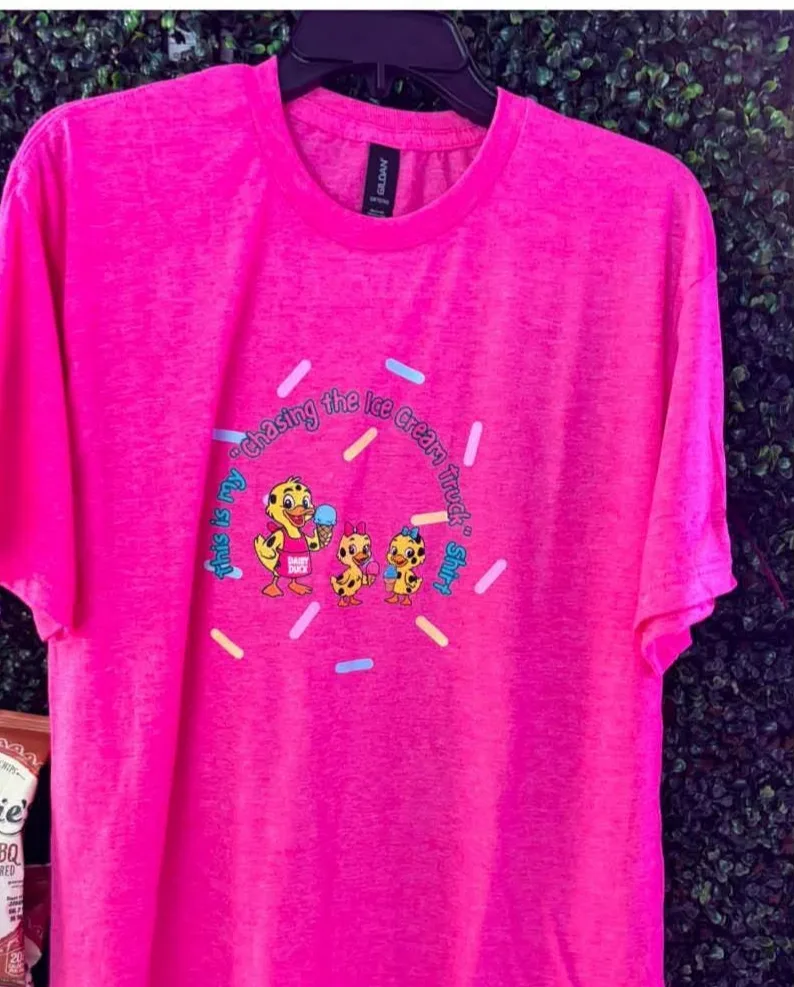 A hot pink t-shirt printed with the three Dairy Duck ducks holding ice creams inside an arc of the words This is my Chasing the Ice Cream Truck shirt, surrounded by scattered pastel sprinkles