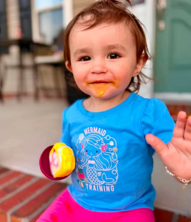 A toddler in a blue shirt waving, holding a treat sitting in a Dairy Duck drip catcher